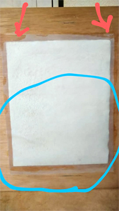 本紙が貼り付いたパネルに、湿らせた裏打ち紙を赤矢印の部分を両手で摘み、近づけ、軽く貼りつけます。